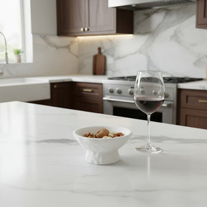 Luna Pedestal Dish Alba Lunarie filled with nuts sits on a white marble kitchen island next to a glass of red wine, with a modern kitchen in the background.