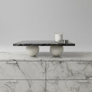 A modern coffee table with a dark gray marble top and two round white stone bases, styled on top of a matching marble cabinet against a light gray background.
