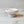 A Solene Pedestal Bowl  lunarie white jewelry display stand with a tiered base, holding a gold ring and a silver ring on a white marble surface.