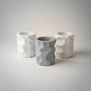 Cave Vessel Jar by Lunarie featuring an organic sculptural texture and matte finish, ideal as a decorative storage vessel for makeup brushes and home decor. Three concrete cave jars with textured surfaces on a plain background