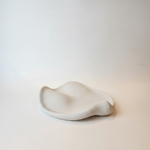 An organic shaped, wavy cement  dish in a matte off-white finish, photographed on a clean, light beige studio surface.