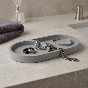 Gray Eclipse Orbit Tray by Lunarie featuring a minimalist dual-circle design, ideal as a decorative catchall tray for jewelry and modern home décor. tray on a bathroom counter with jewelry, including rings and a chain.