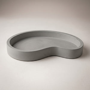 Moonlit Arc Tray by Lunarie featuring an elegant organic shape and minimalist matte finish, ideal as a decorative catchall tray for jewelry and home décor. Gray wavy concrete dish on a beige background