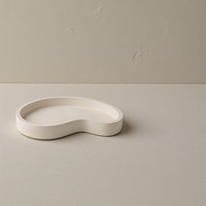 Moonlit Arc Tray by Lunarie featuring an elegant organic shape and minimalist matte finish, ideal as a decorative catchall tray for jewelry and home décor. White, wavy concrete dish on a beige surface with a plain background