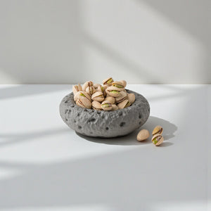 Moonstone Hollow Bowl by Lunarie featuring a moon-inspired textured surface and organic sculptural design for modern home décor.  place it with Pistachios in a gray concrete bowl on a white surface with soft shadows
