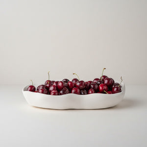 Nest Centerpiece Bowl by Lunarie featuring an organic sculptural shape with flowing curves, ideal as a decorative centerpiece bowl for modern home décor.  filled with red cherries on a light gray background