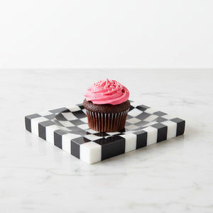 Noir Blanc Checkered Trinket Dish by Lunarie crafted from natural marble with a black and white checkered pattern and wavy sculptural design. with Chocolate cupcake with pink frosting on it.