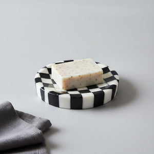 Noir Blanc Checkered Trinket Dish by Lunarie crafted from natural marble with a black and white checkered pattern and wavy sculptural design with a Bar of soap on it  on a light gray background