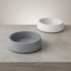 Two  small  orbit  concrete bowls, one gray and one white, on a light gray surface.